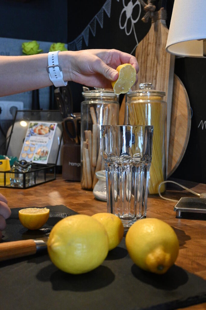 Frische Zitrone wird in ein Glas gepresst, um ein gesundes Getränk zuzubereiten.