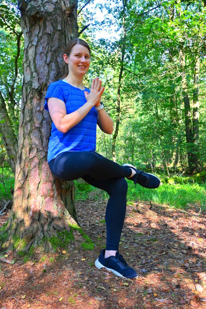 Simone praktiziert eine Yoga-Pose im Wald, angelehnt an einen Baum, als Symbol für Balance und Verbundenheit mit der Natur.